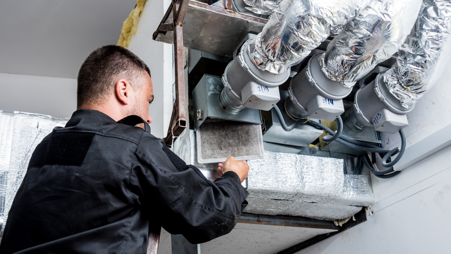 A man is working on a ventilation system in a building.
