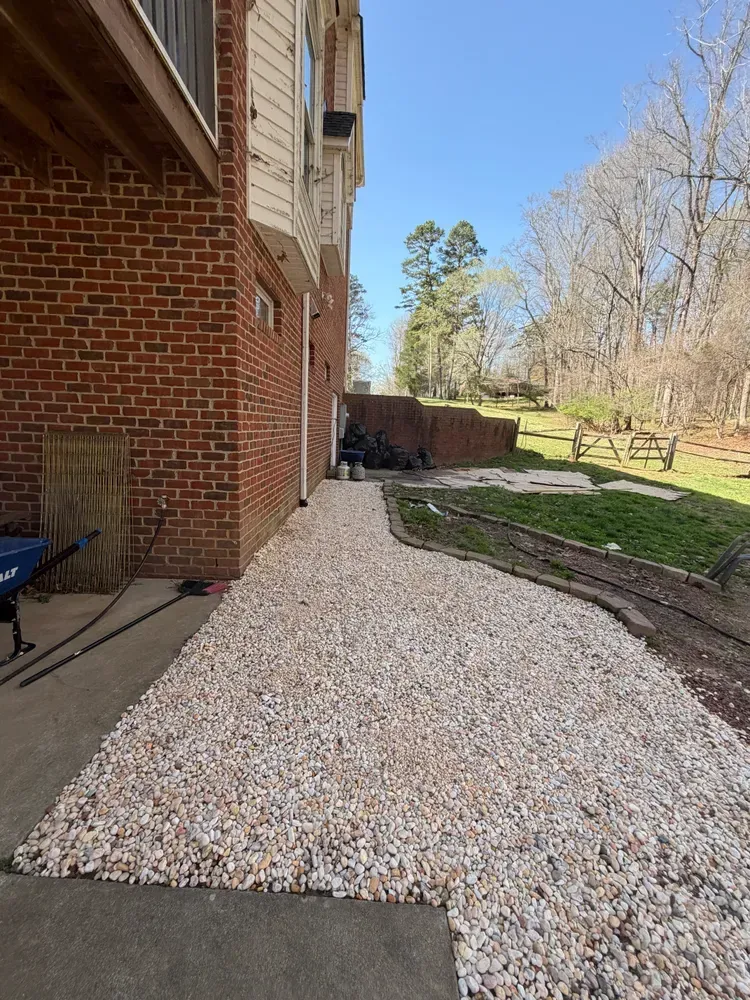 Brick house exterior with a white gravel walkway beside a landscaped yard and trees