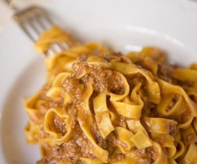 Fettuccine al ragù su un piatto bianco; una forchetta è parzialmente infilata.