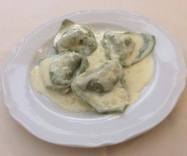 Tortellini verdi in salsa bianca cremosa su un piatto bianco.