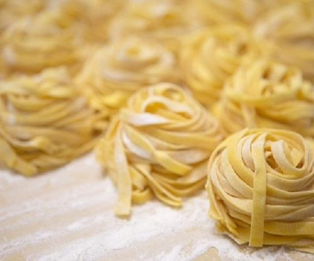 Nidi di pasta fresca su una superficie infarinata, con uova e farina sullo sfondo.