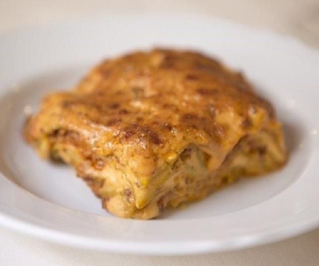 Lasagna su un piatto bianco, dorata, con formaggio fuso.