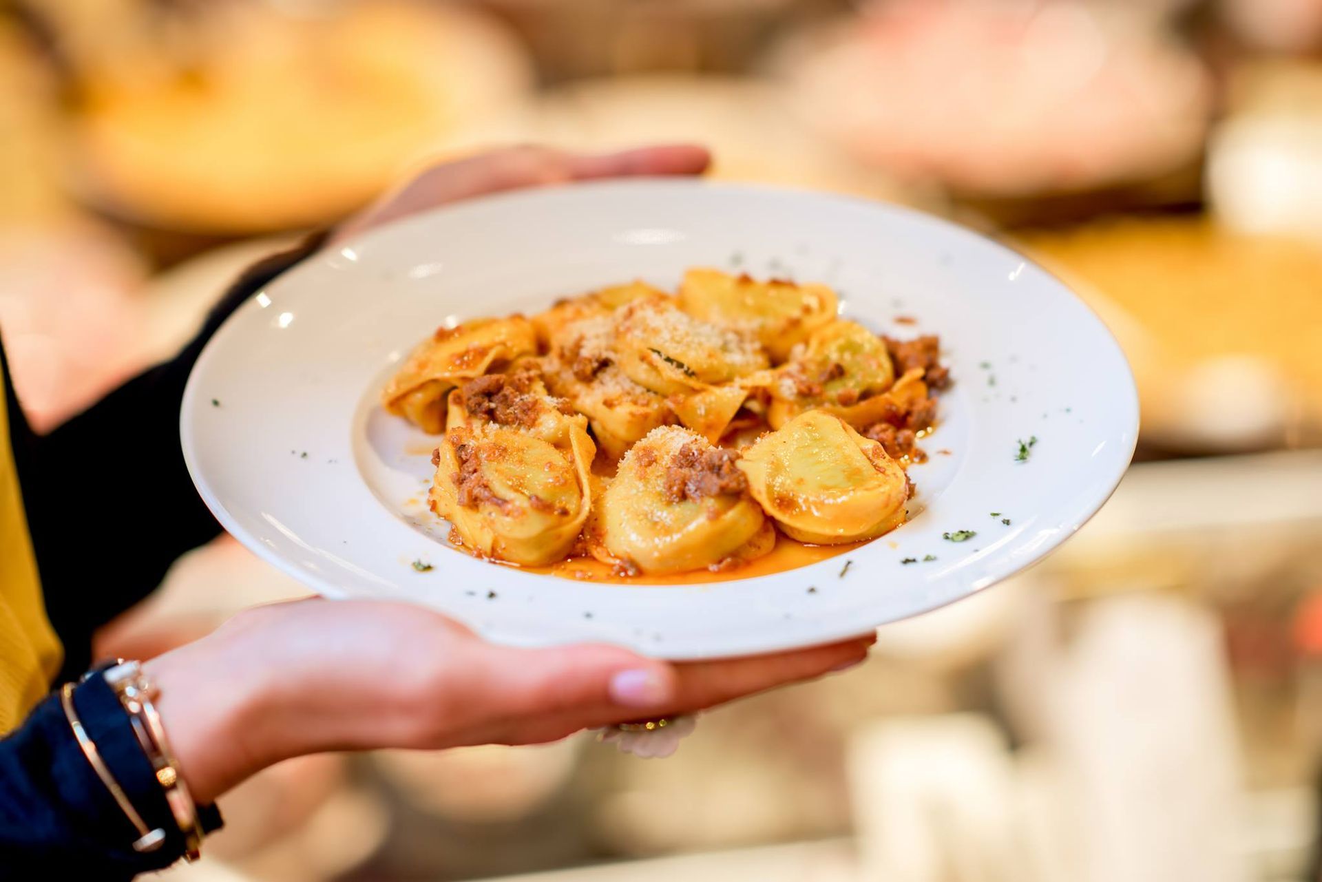 Persona che tiene in mano un piatto bianco di tortellini con sugo di carne.