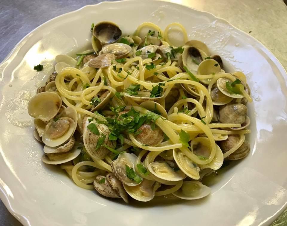 Spaghetti alle vongole: piatto di pasta con vongole, erbe aromatiche e limone in una ciotola bianca.