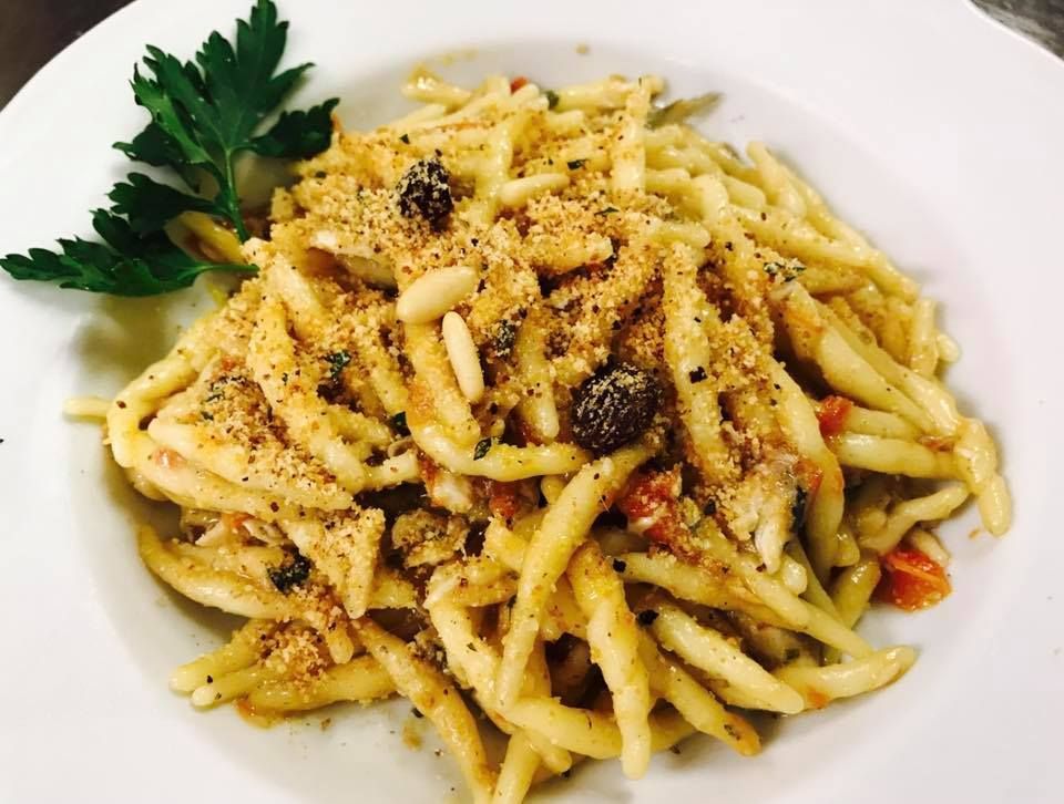 Piatto di pasta, guarnito con pangrattato, uvetta, pinoli e prezzemolo su un piatto bianco.
