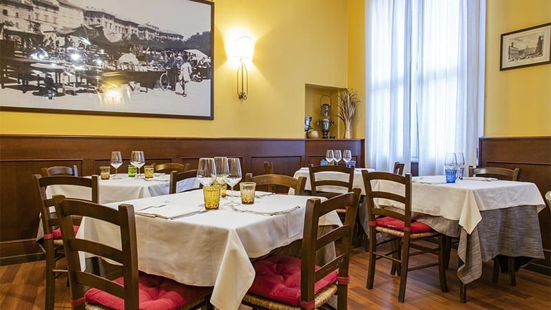 Sala da pranzo con tavoli apparecchiati per il servizio, pareti gialle, pannelli in legno e una grande fotografia in bianco e nero.