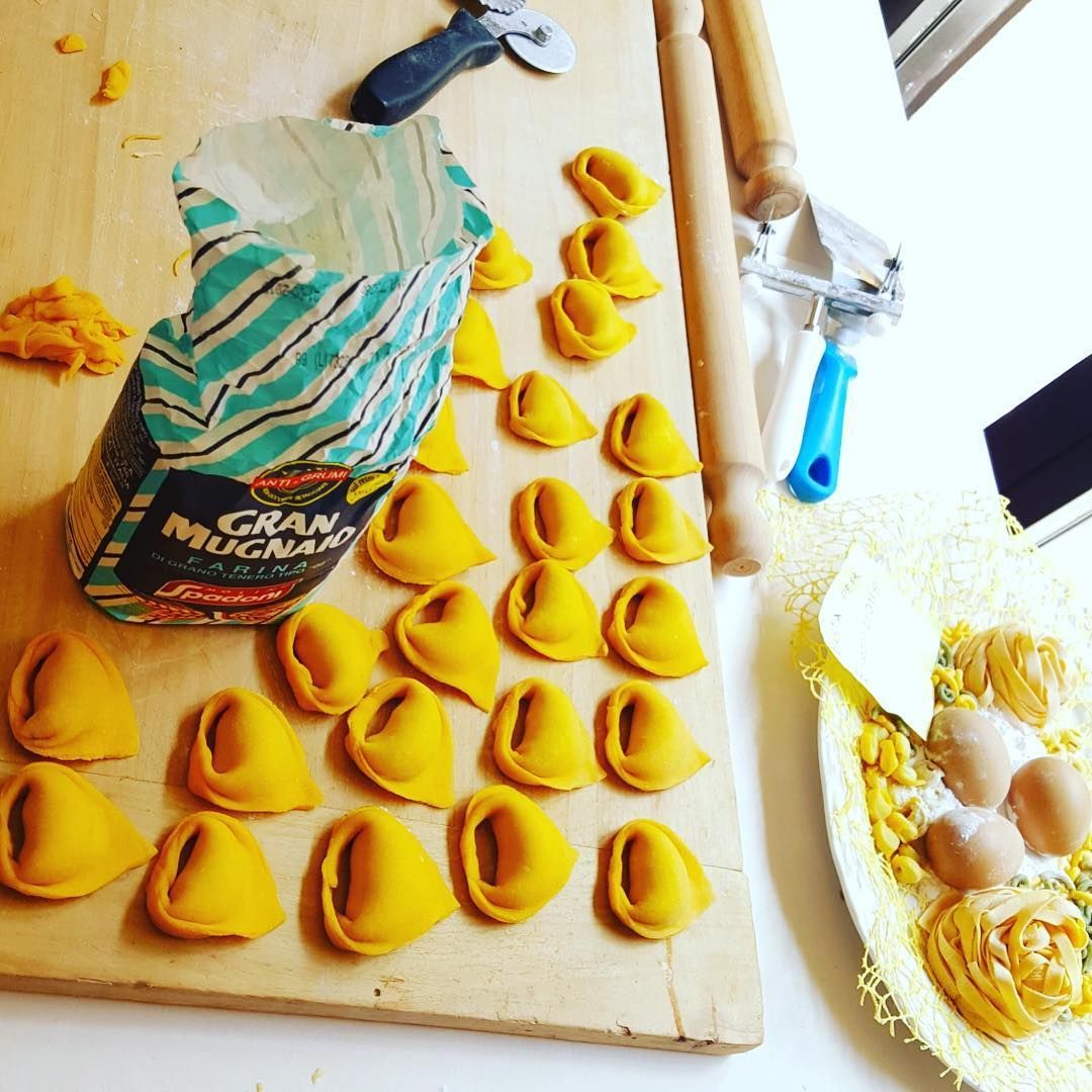 Scena di preparazione della pasta fatta in casa: tortellini disposti su un tagliere di legno con farina e ingredienti come le uova.