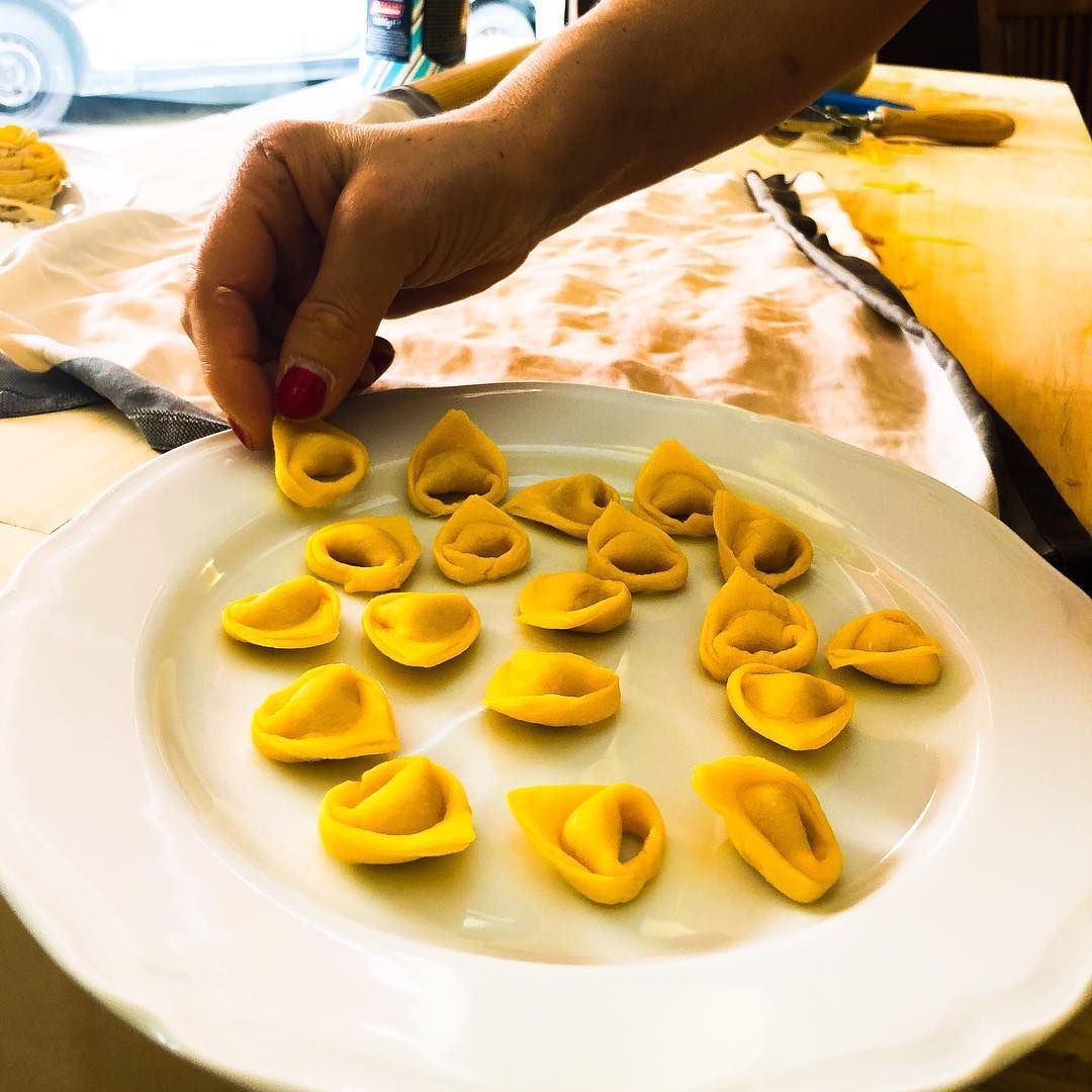 Persona in canottiera che stende un foglio di pasta rosa su una superficie bianca, con il mattarello nelle vicinanze.
