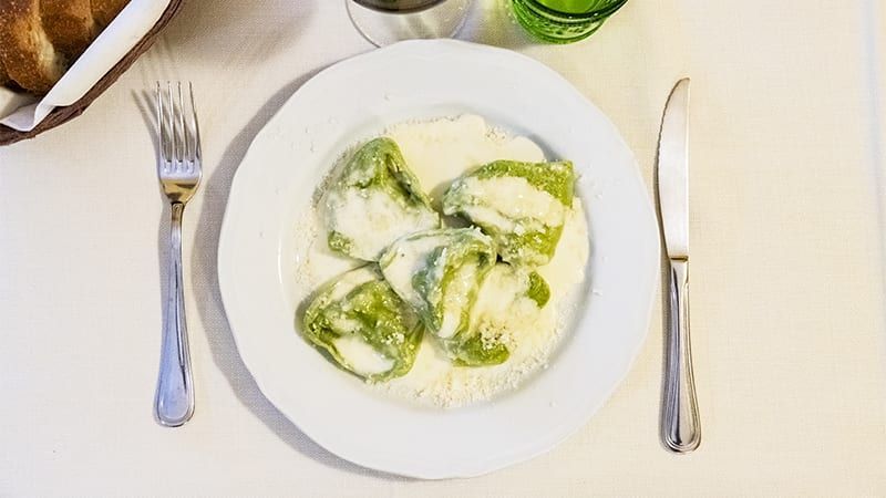 Piatto di pasta verde con salsa cremosa, posate su una tovaglia bianca.