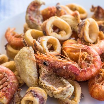 Mucchio di frutti di mare fritti, tra cui gamberi e anelli di calamaro, su un piatto bianco.