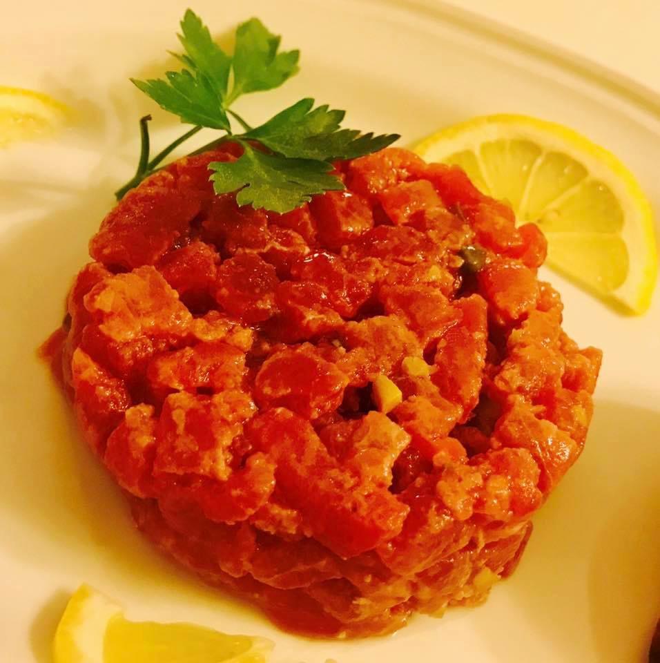 Una porzione di tartare di tonno, guarnita con prezzemolo e fettine di limone.