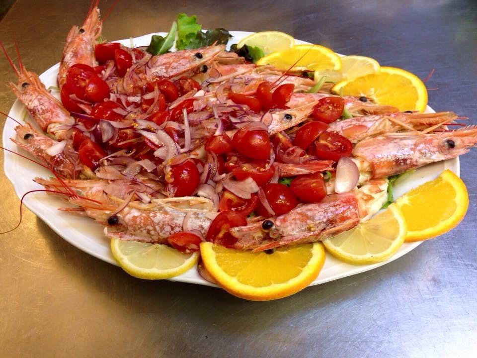 Piatto di gamberi cotti guarnito con pomodori, cipolle, fette di limone e arancia.