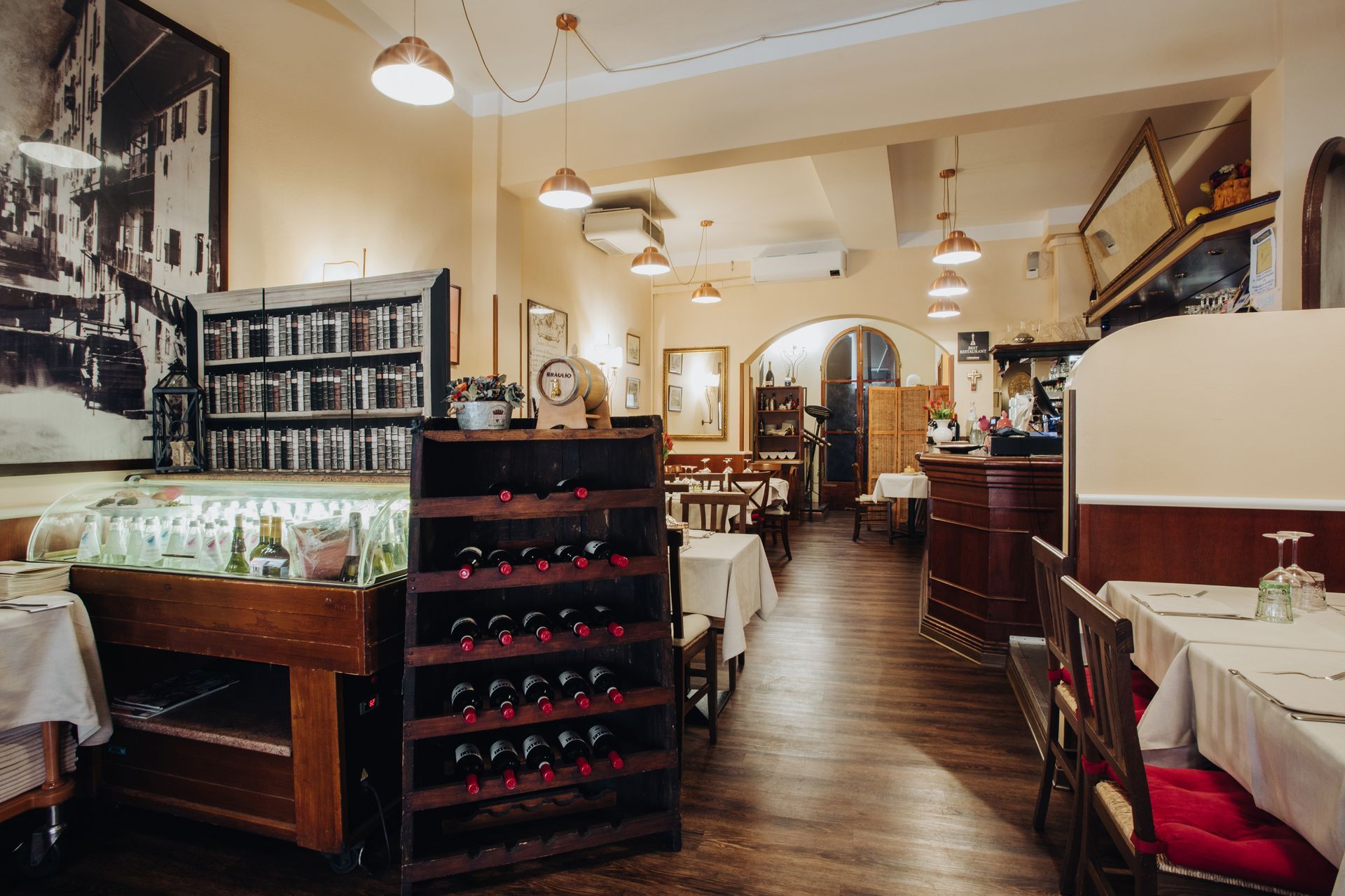 Interno di un ristorante con tavoli, portabottiglie, opere d'arte e lampade a sospensione.