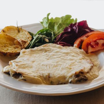 Pollo alla parmigiana con patate arrosto, insalata e fette di pomodoro su un piatto bianco.