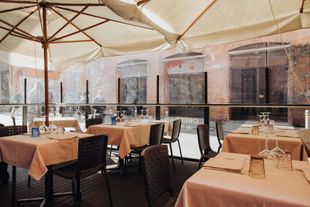 Patio del ristorante con tavoli apparecchiati per cenare, sotto un ombrellone. La luce del sole filtra a fiotti.