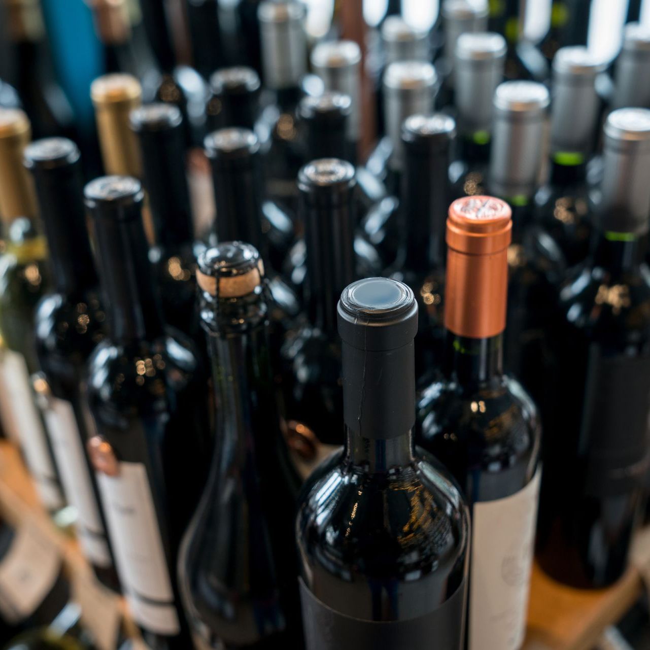Bottiglie di vino di vari stili, alcune con tappo di sughero, altre con tappo a vite, in una disposizione ravvicinata.