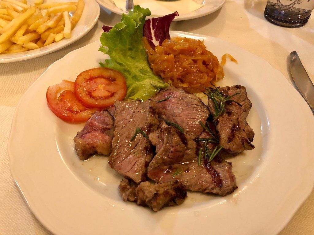 Piatto con bistecca tagliata a fette, pomodori, verdure e cipolla fritta.