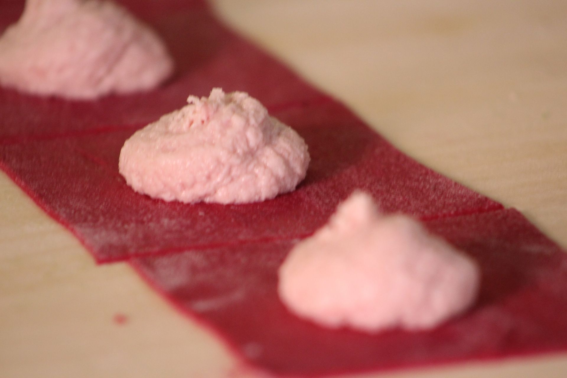 Ripieno rosa adagiato su una sfoglia di pasta rossa, pronto per essere piegato a formare i ravioli.