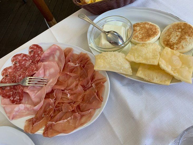 Piatto di salumi con pasta fritta, pane piatto, burro e salsa su una tovaglia bianca.