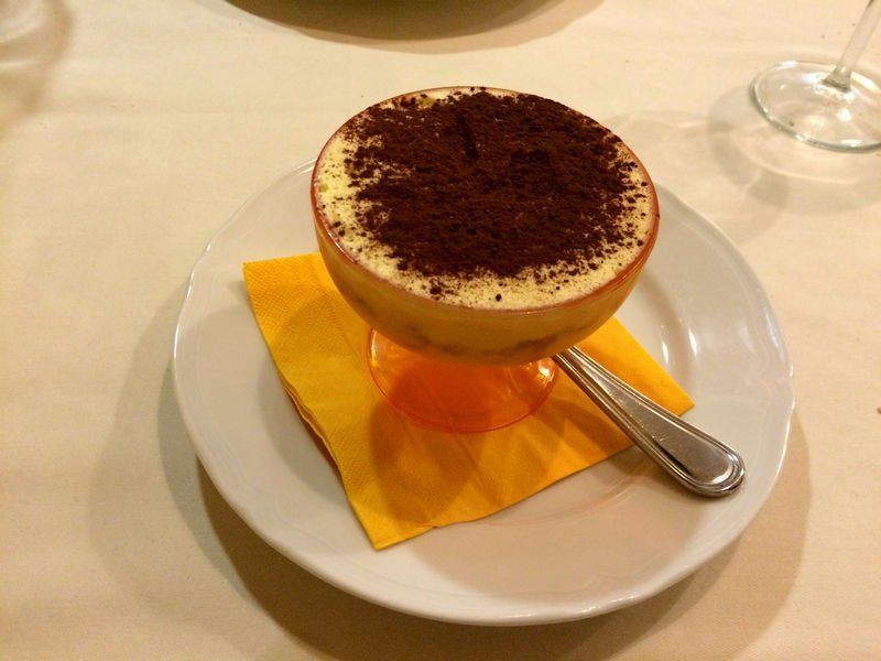 Tiramisù servito in un bicchiere con stelo, su un piatto con tovagliolo e cucchiaio.