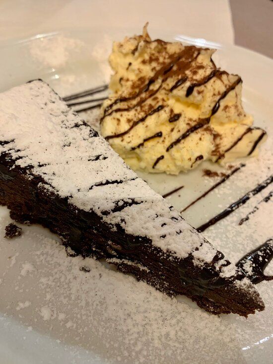Fetta di torta al cioccolato con zucchero a velo e panna montata, guarnita con cioccolato.