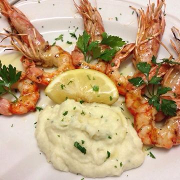 Gamberi alla griglia con limone e purè di patate, guarnito con prezzemolo.