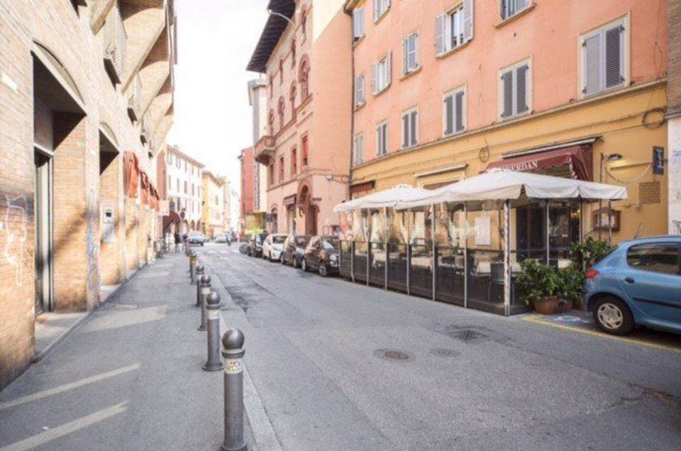 Strada acciottolata a Bologna, Italia, fiancheggiata da edifici e da un ristorante con tavoli all'aperto.