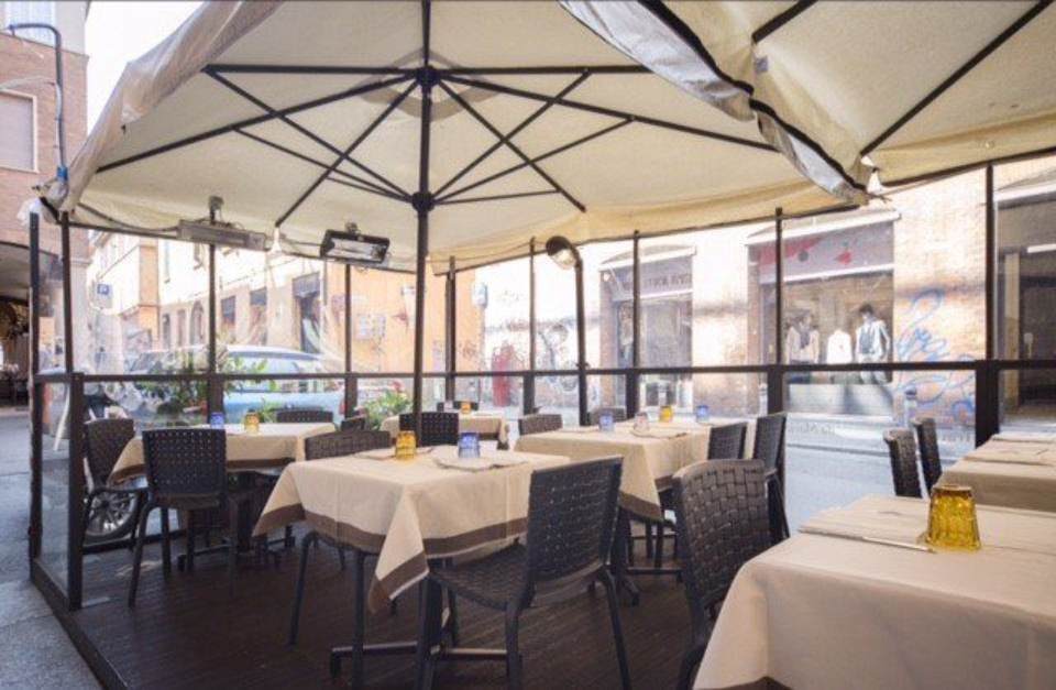 Ristorante con posti a sedere all'aperto sotto un grande ombrellone e tavoli apparecchiati per cenare.
