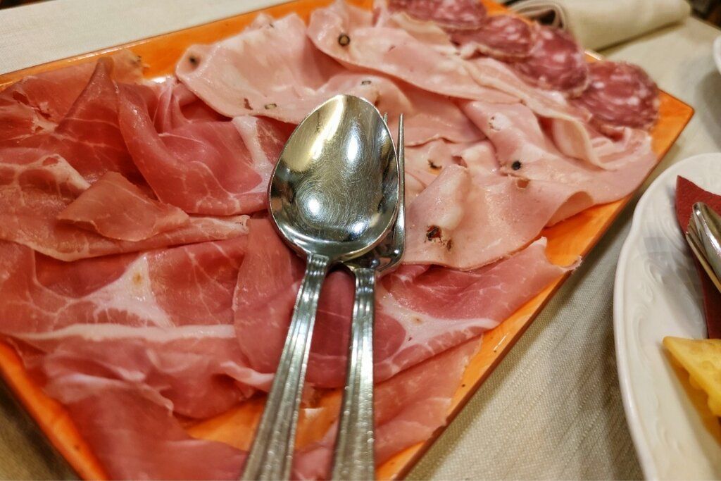 Piatto di carne con prosciutto, mortadella e salame, servito con posate.
