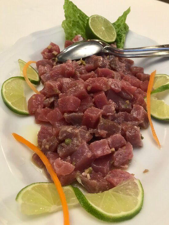 Piatto di tonno crudo, tagliato a cubetti, guarnito con fette di lime, nastri d'arancia e lattuga su un piatto bianco.