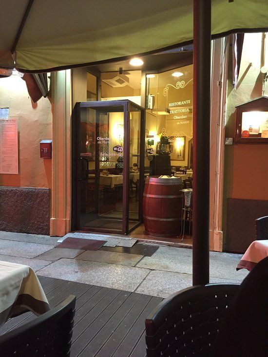 Ingresso del ristorante di notte con porte in vetro, una botte di legno e posti a sedere all'aperto.
