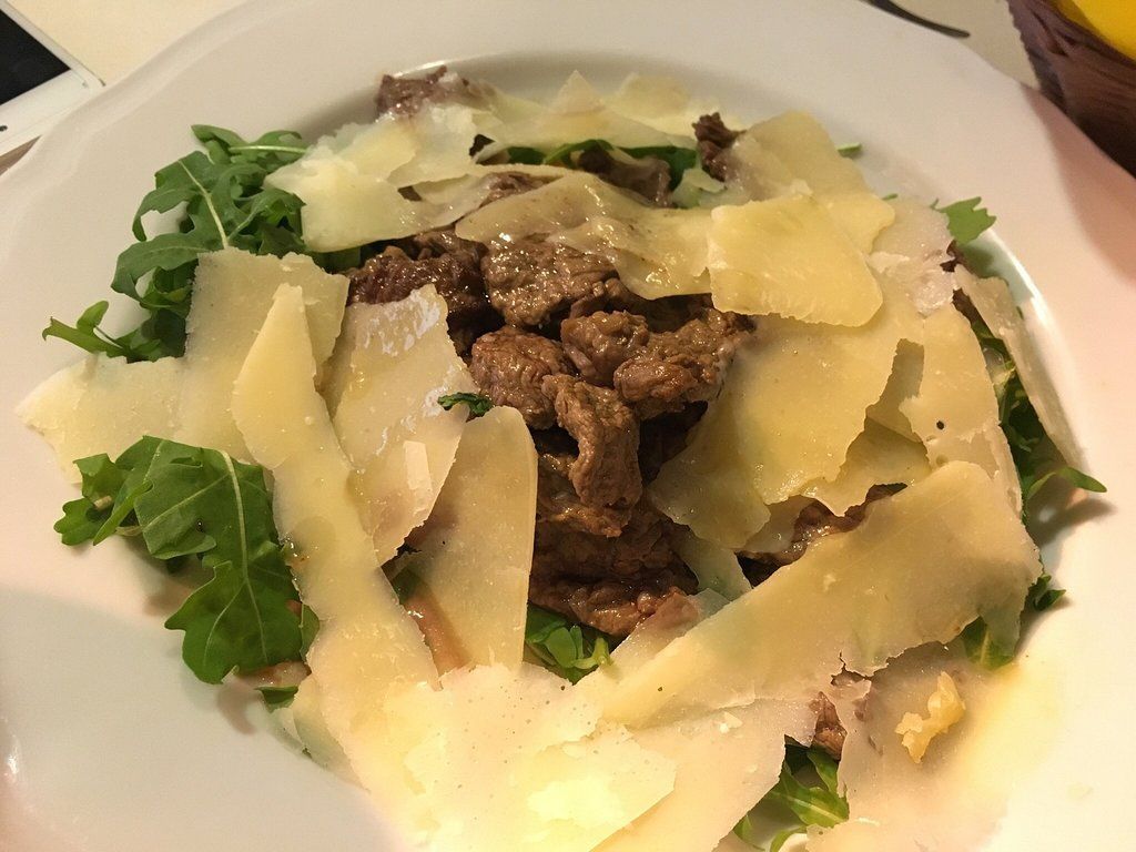 Insalata con rucola, parmigiano grattugiato e manzo su un piatto bianco.