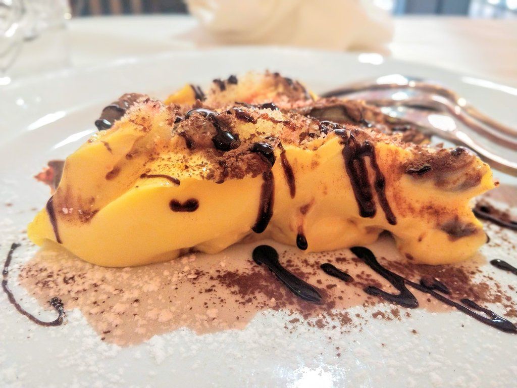 Dolce giallo con gocce di cioccolato e cacao in polvere su un piatto bianco.