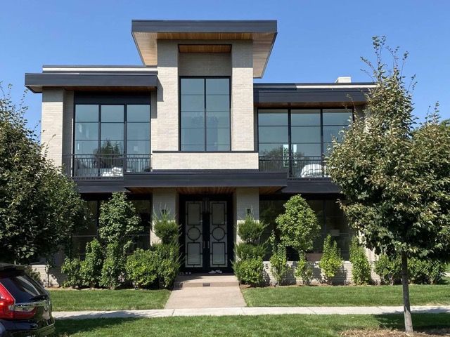 Modern two-story house with large windows, dark trim, and a manicured front yard