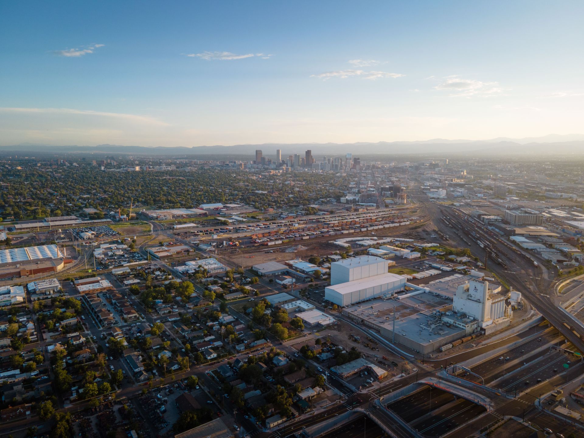 Aerial view of a city skyline at sunset with rail yards, roads, and industrial buildings in the foreground