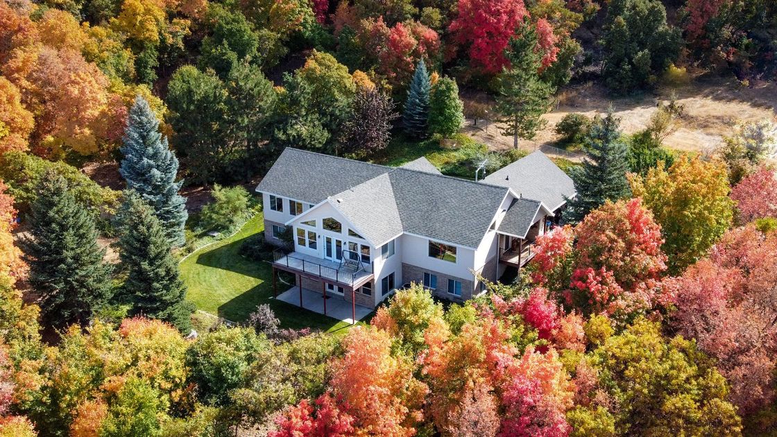 Aerial view of a white house with a gray roof nestled among colorful autumn trees.