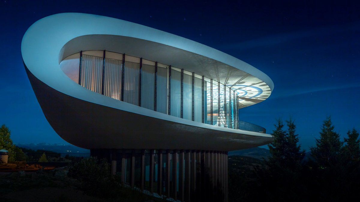 Modern futuristic white building with curved roof and large glass facade at dusk