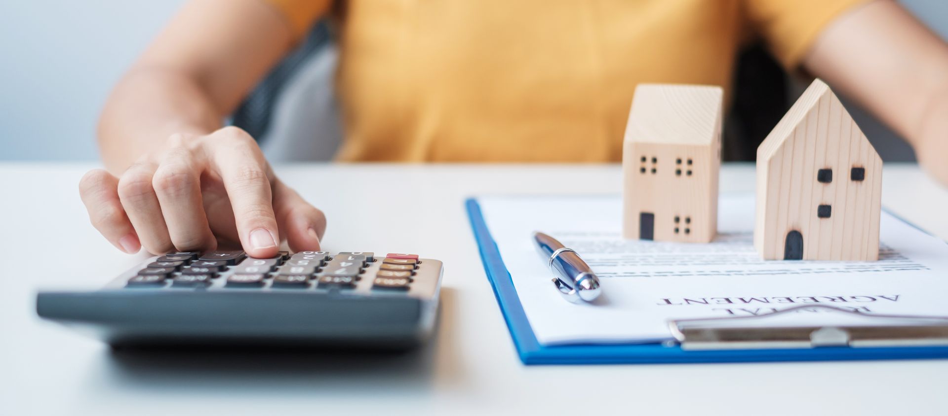 Hand using calculator beside house models and paperwork on a desk