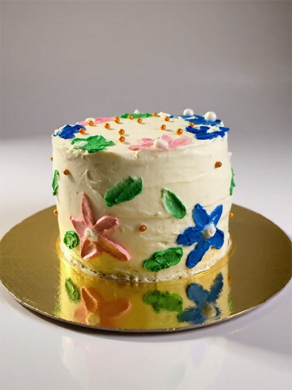 Pastel decorado con flores glaseadas en tonos rosa, azul y verde sobre una base dorada.