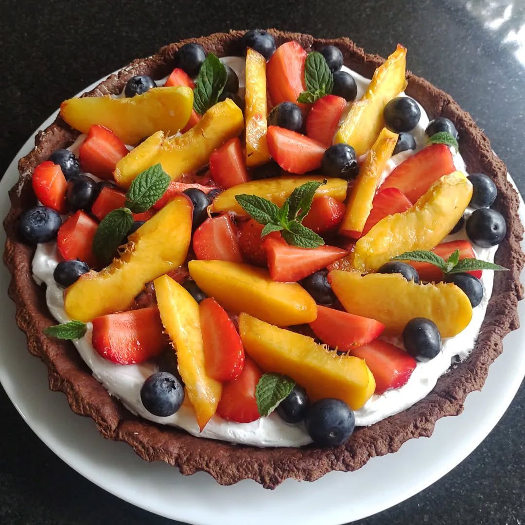 Tarta de chocolate con crema batida, cubierta con duraznos, fresas, arándanos y menta.