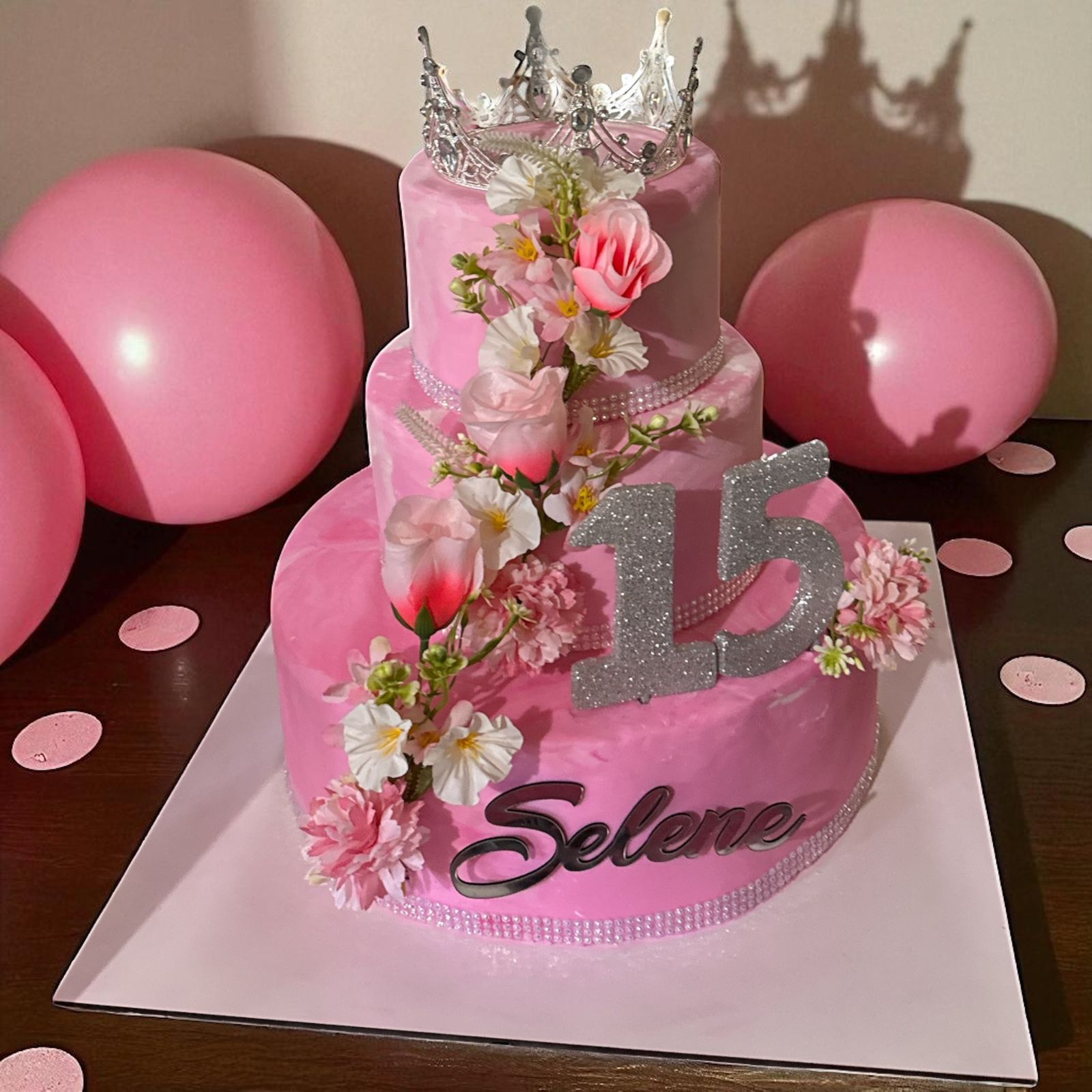 Pastel de cumpleaños rosa de tres niveles con flores, corona, brillantina