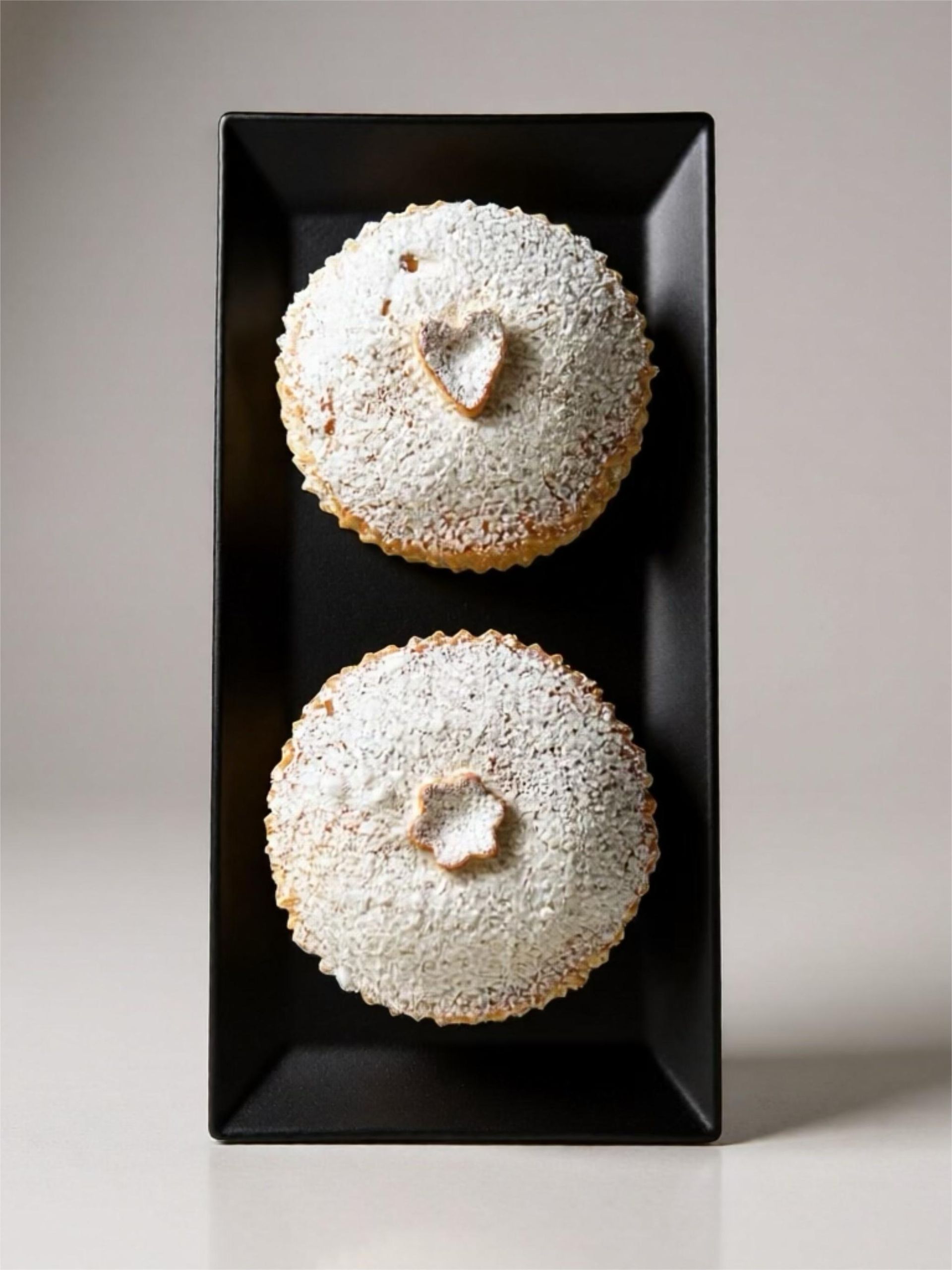 Dos tartas cubiertas con forma de corazón y espolvoreadas con azúcar glas sobre un plato rectangular negro.