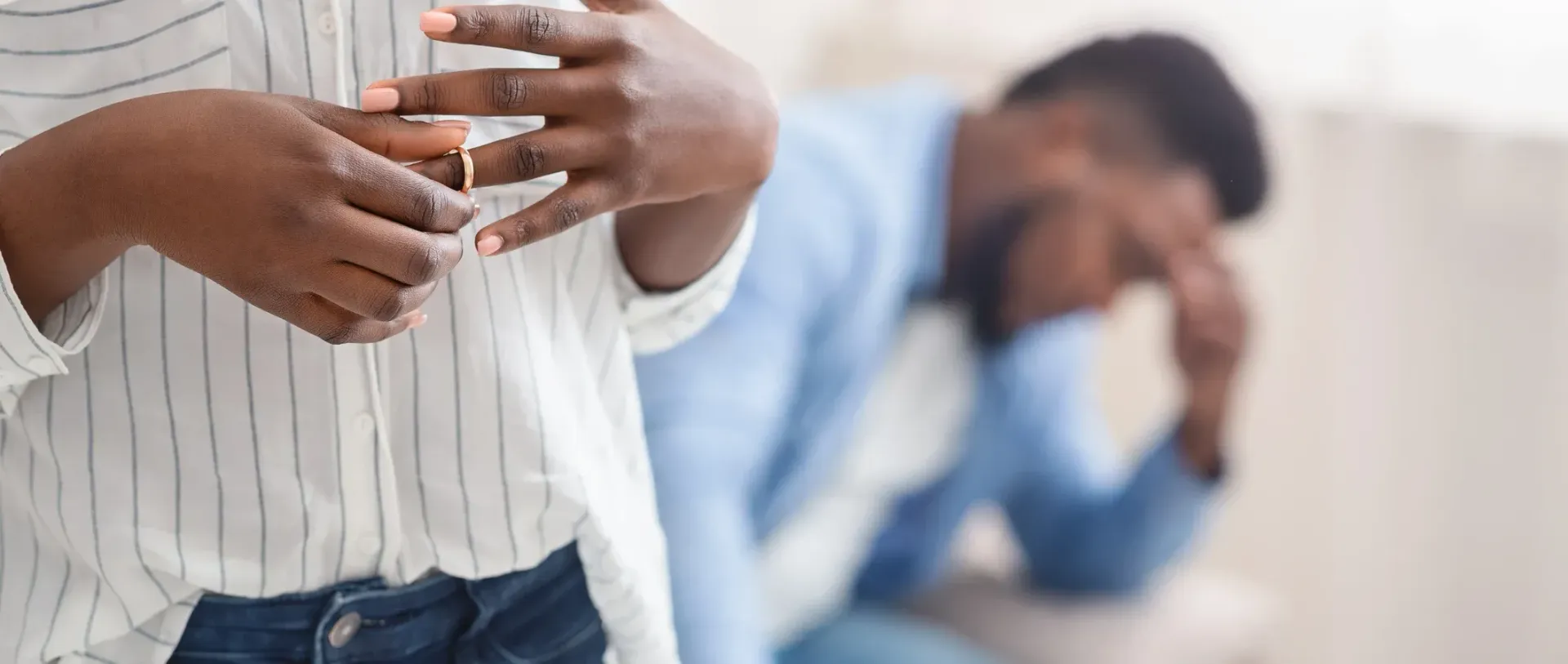 A man is sitting on a couch with his head down while another man stands behind him.