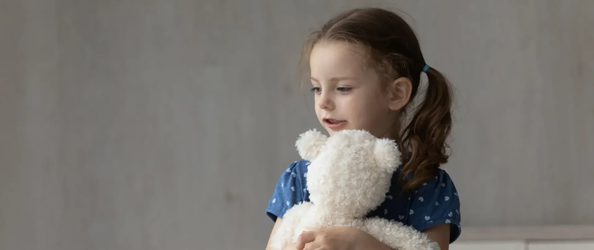 A little girl is holding a white teddy bear in her arms.