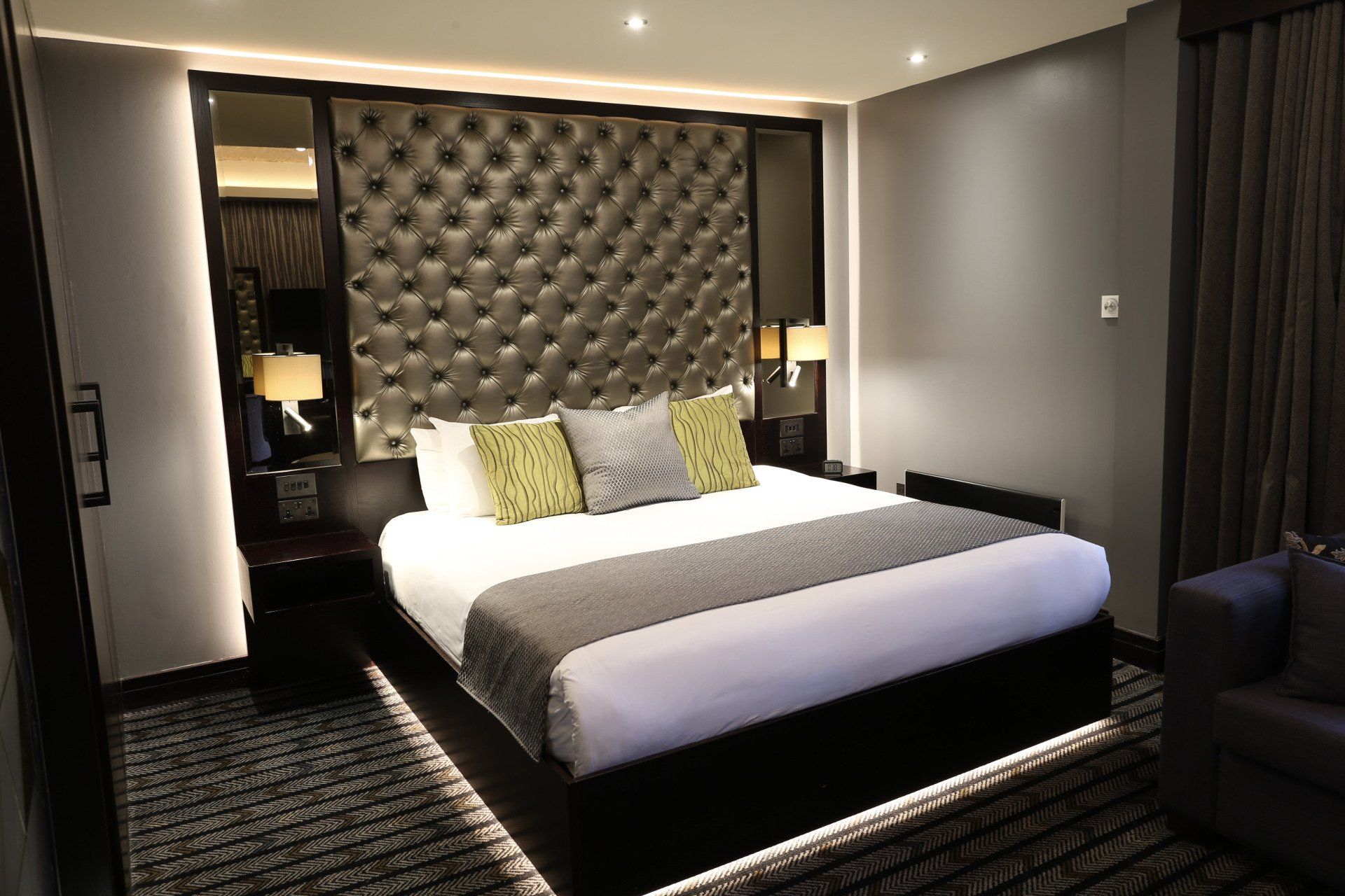 Bedroom with a large bed, tufted headboard, and ambient lighting; gray and brown color scheme.