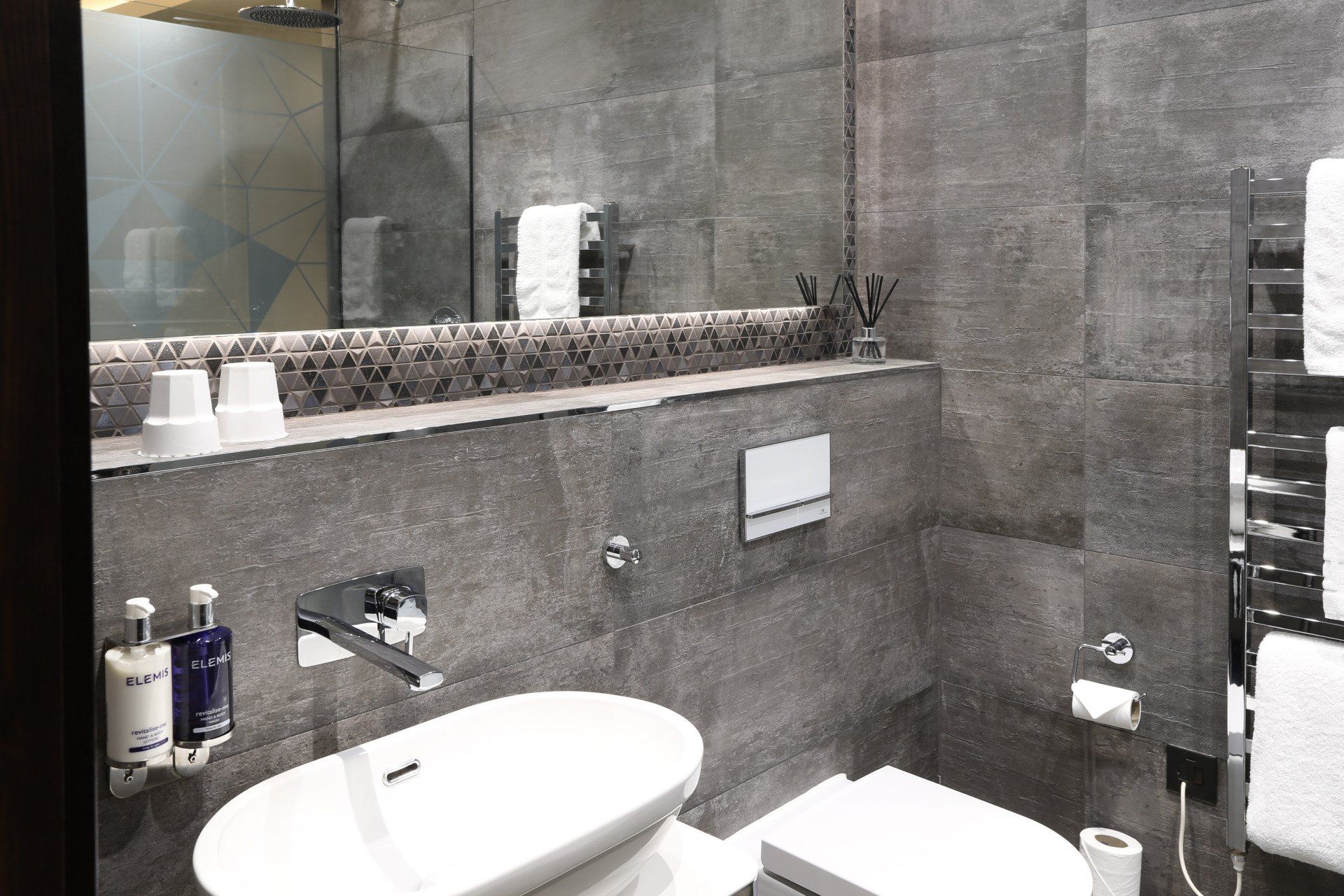 Modern bathroom with grey tile walls, white sink and toilet, and a towel warmer.