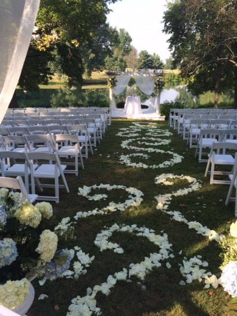 A wedding aisle with white chairs and petals on the ground