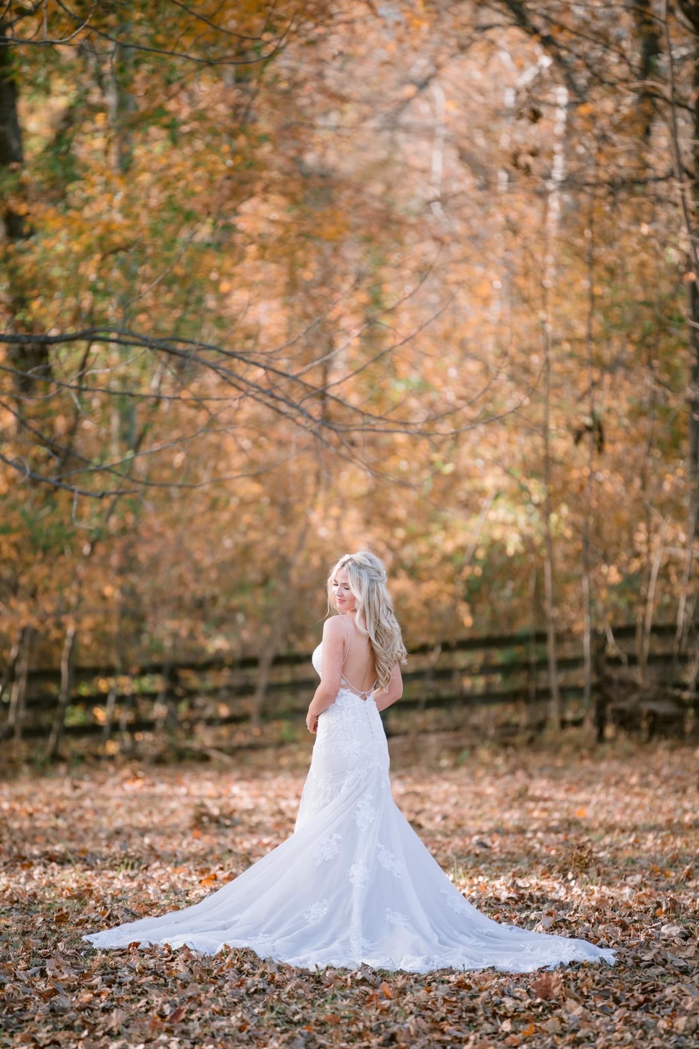 A bride in a wedding dress is standing in a pile of leaves in the woods.