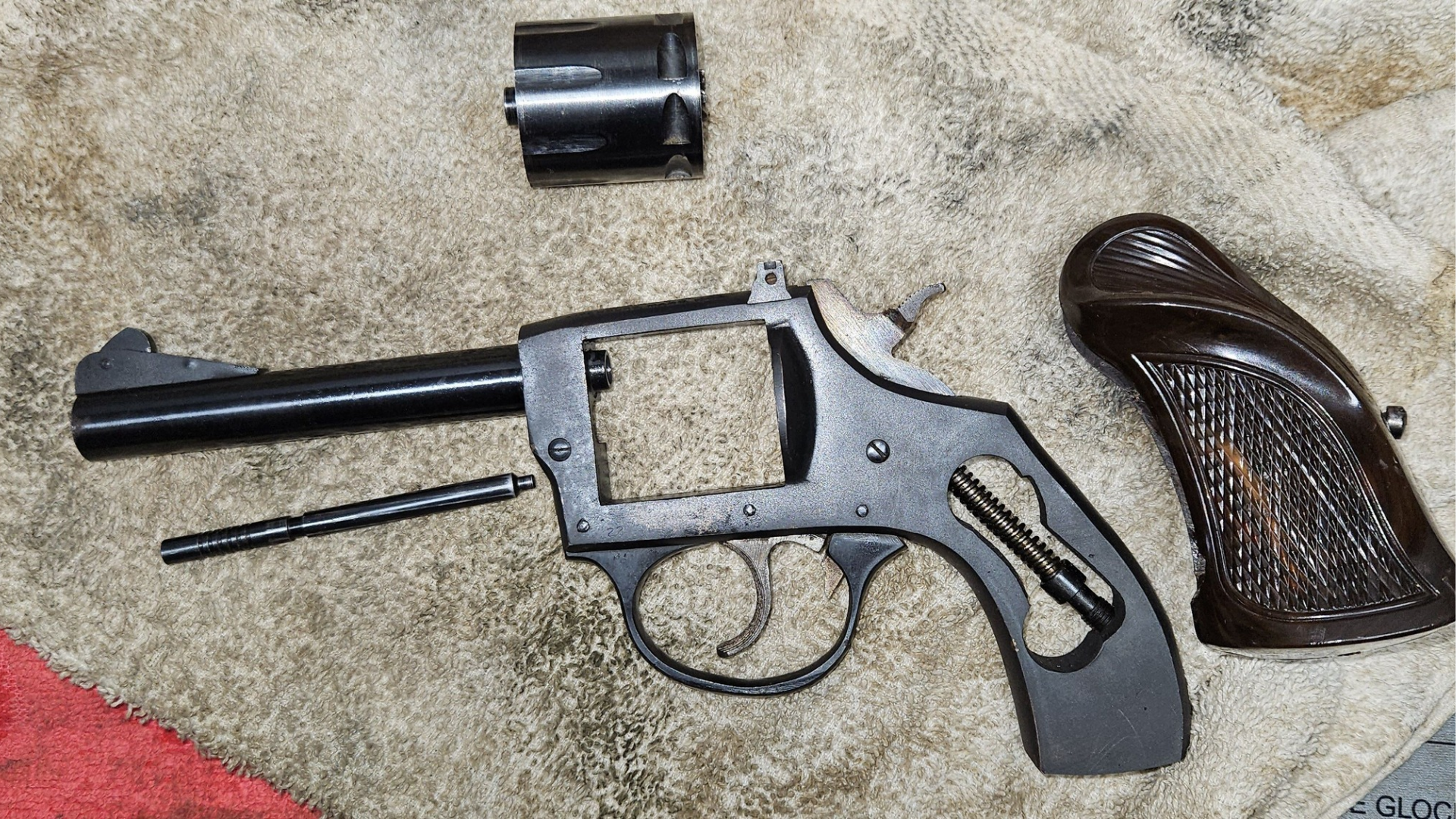 Disassembled black handgun parts laid on carpet, including frame, barrel, cylinder, and grip panel.