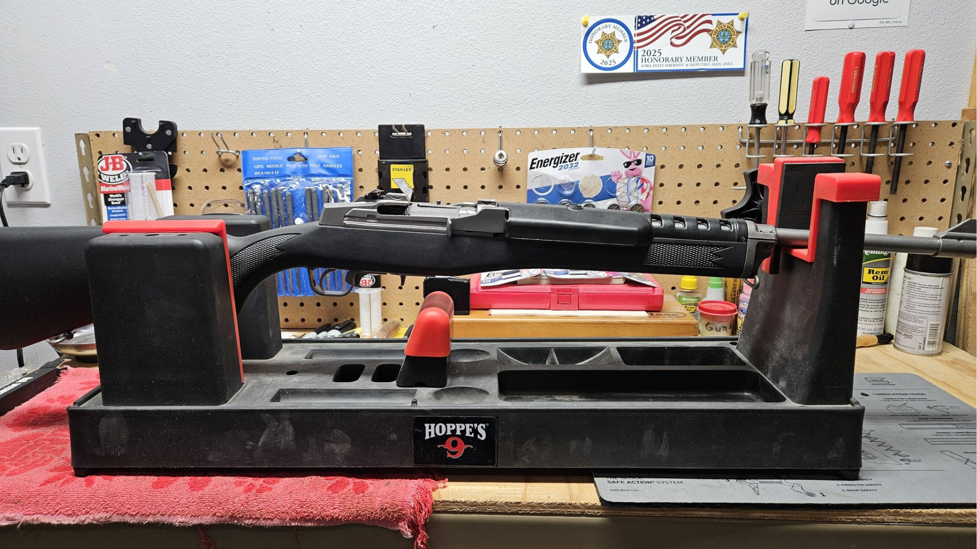 Black metal tool on a red workbench in a workshop, with shelves of parts and tools in the background
